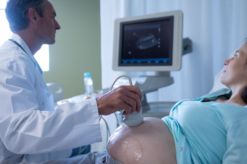 Caucasian male doctor doing ultrasound scan for pregnant woman in hospital